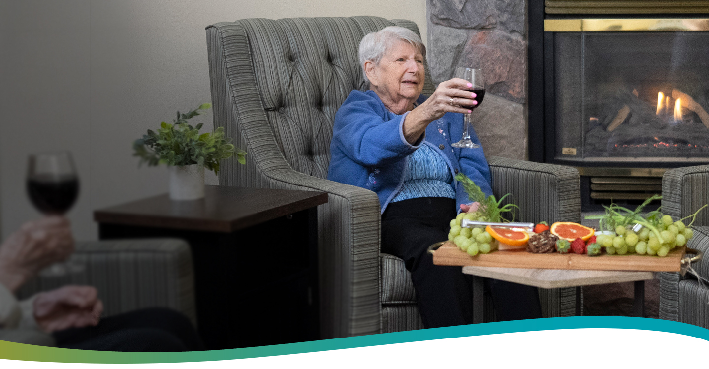 Resident Betty relaxing with a glass of wine by the fireplace at Atrium Retirement Residence in Orillia.